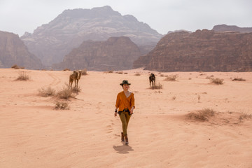 Fototapeta na wymiar cowboy in a hat and boots is walking on the sand in the desert in the background of the camels.