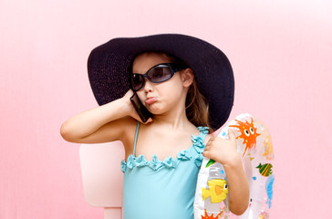 little girl in a swimsuit and hat is talking on the phone