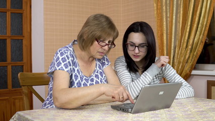 Daughter teaches mother how to use a laptop. A young woman shows her old mother where to click on a...