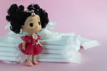 Feminine sanitary napkin, an absorbent item worn by a woman while menstruating, with blurred lady doll on pink background for hygiene and health concept