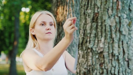 Young woman attaches an ad to a tree in the park