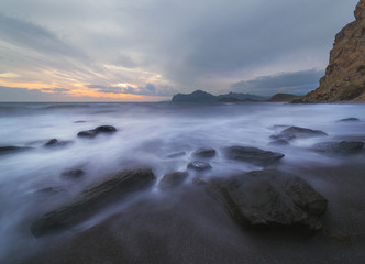 Fototapeta na wymiar Seascape with stones ashore mountains on the horizon and gray sky