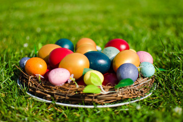 Easter eggs pictured in a wooden basket on green grass.