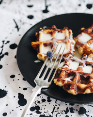 An excellent early Breakfast. Viennese Belgian waffles decorated with flowers on a black plate, a mug of black tea and vintage Cutlery on the table. White background and black and white tablecloth