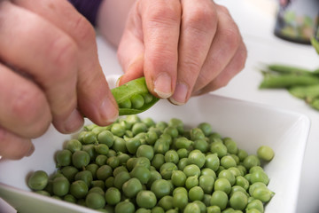 Closeup of hands of woman peeling fresh organic peas on white table background