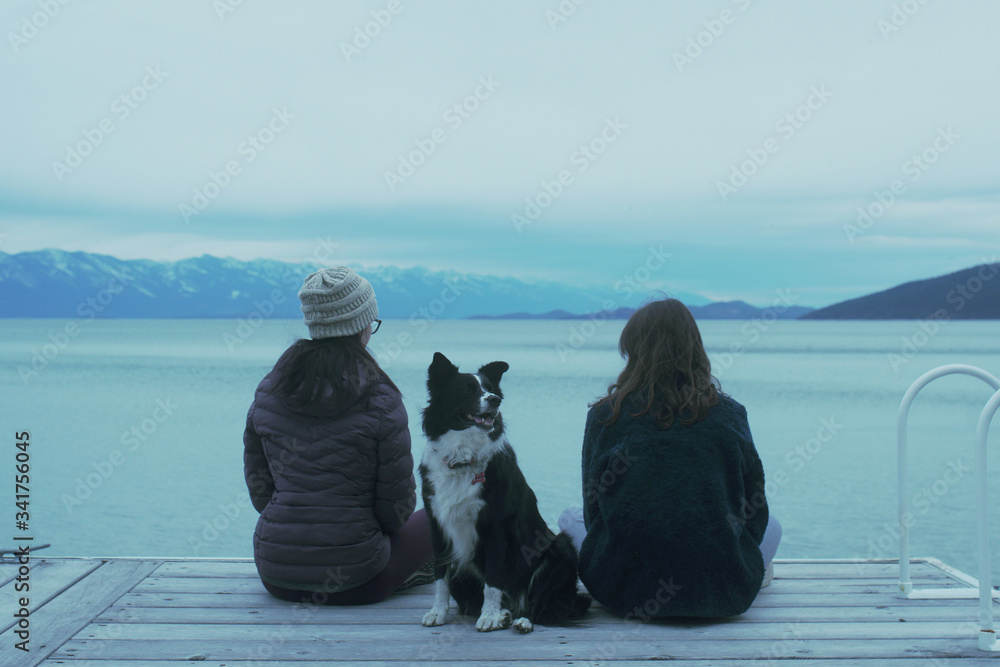 Wall mural sisters and their border collie dog sitting on a dock