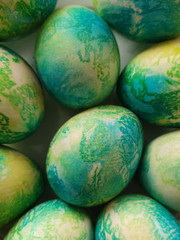Many (mint) blue yellow eggs similar to dragon eggs, painted in colored dyes, lie on a white background.