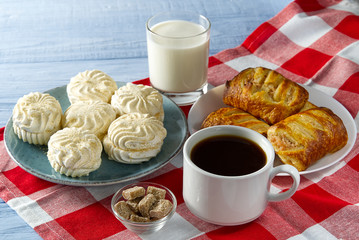 Cup of americano coffee and homemade zephyr or marshmallow in a blue plate on light blue wooden...