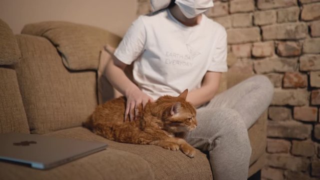 Funny woman with face mask and towell pets orange cat