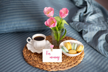 Fototapeta na wymiar Mothers Day. Breakfast in bed for mom. Breakfast in bed with a map and a cup of coffee. Macarons with a cup of coffee. Good morning. Greeting card for mom. Tulips Unmade pastel with breakfast