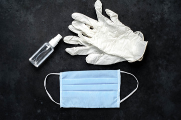 white medical gloves, surgical mask and hand disinfector, protection against coronavirus on stone background