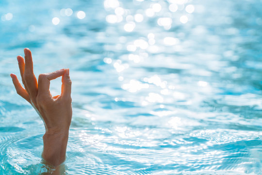 Woman hand make a sign, OK on the background of azure sea water and the glare of the sun. Female hand shows gesture OK. OK Hand sign. 