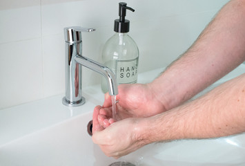 Closeup of a man washing hands with soap under the faucet with water.