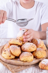 Homemade Hot buns with raisins on a wooden board. The child holds a bun in his hands and sprinkled with icing sugar. Baking fresh from the oven