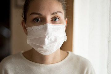 A young woman in a medical mask stands near the window