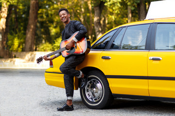 Portrait of handsome trendy multiple race young man in casual clothes near yellow vintage car, play...