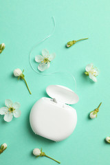 Dental floss and flowers on mint background, top view