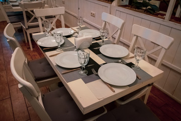 : The served table in the restaurant. Clean dishes and appliances on the tablecloth in a cafe. Shiny transparent glasses. White plates. Prepared for the reception of guests. High service.
