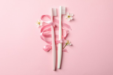 Toothbrushes, ribbon and flowers on pink background, space for text