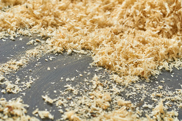Scattered wooden sawdust on dark concrete surface in carpentry workshop