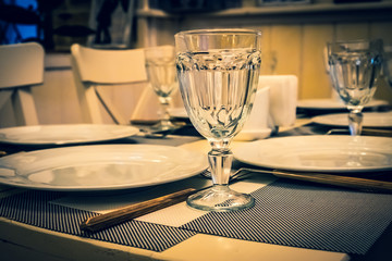 : The served table in the restaurant. Clean dishes and appliances on the tablecloth in a cafe. Shiny transparent glasses. White plates. Prepared for the reception of guests. High service.