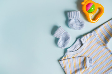 Baby undershirt, booties and rattle on blue background. Copy space. Clothes of newborn boy.