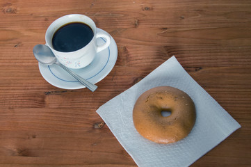 a cup of coffee with a bagel on a napkin, isolated on a wooden background