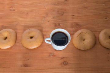 several bagel  and a cup of coffee seen from above, formed a straight line, isolated on wooden...