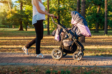 Mother's day. Young woman walking in spring park with baby carriage. Mother spends time with her...