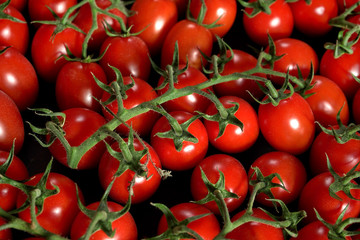 Heap of small bright cherry red tomatoes with green vine leaves, closeup detail from above