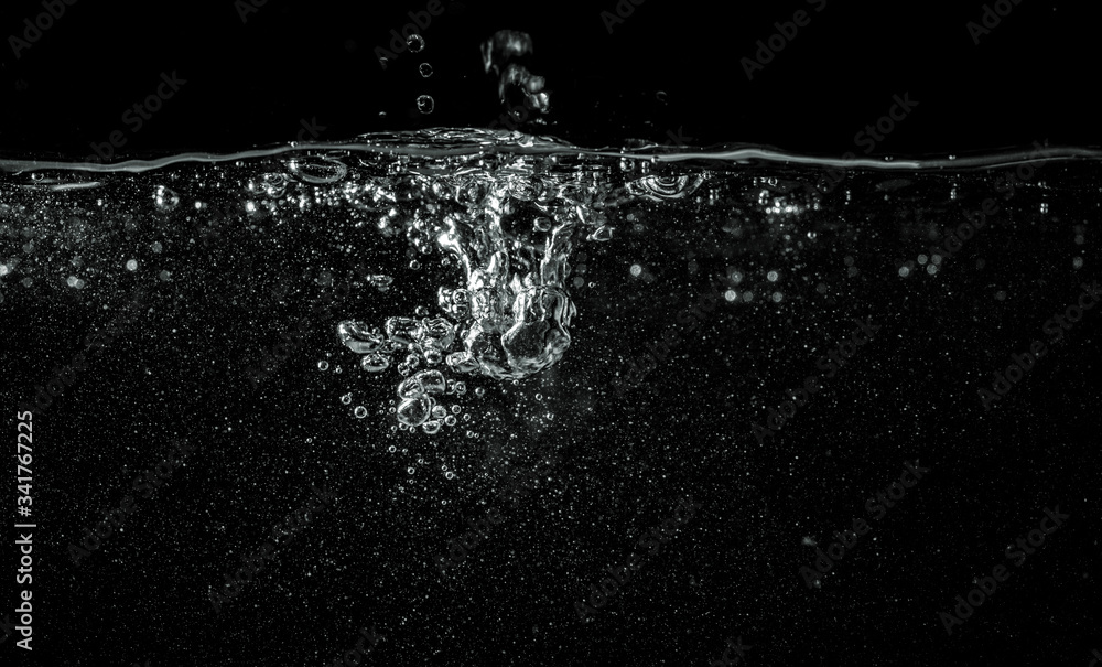 Wall mural Water pouring into aquarium, black background, detail on dropped liquid creating white bubbles and abstract shapes