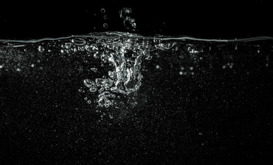 Water pouring into aquarium, black background, detail on dropped liquid creating white bubbles and...