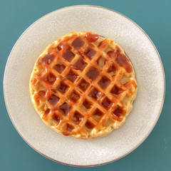 top view on waffle covered in caramel/dulce de leche on a white plate over a blue table