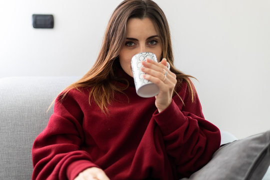 Young woman having a hot drink witting on her sofa