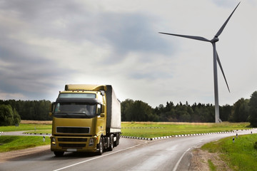  yellow truck is driving a wind turbine behind it, trade and logistics - in the backgrounds windmills