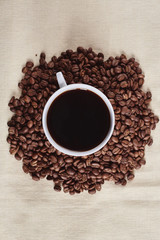 A Cup of espresso coffee drink on a handful of roasted brown coffee beans