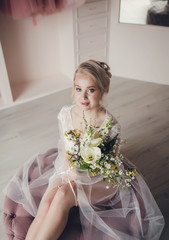 Pretty bride in a white wedding dress with a bouquet of flowers in studio