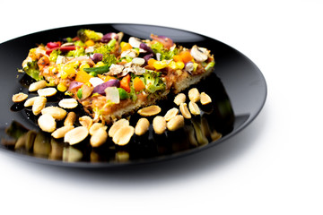 Homemade vegan pizza with vegetables on black plate, white background.
