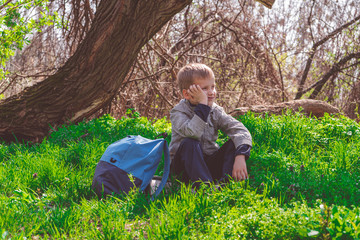 Solo traveller - young boy hiker in spring forest, sitting on green grass and looking thoughtfully into the distance