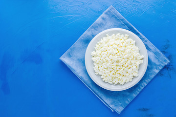 Cottage cheese in a white plate on a blue background. Organic eco healthy meal, dairy product. Plate of cottage cheese on a blue napkin. Top view. Copy space