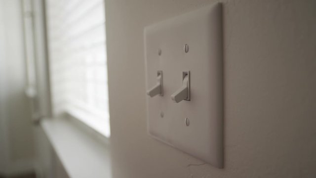 A person turns off a light switch during the day inside a home