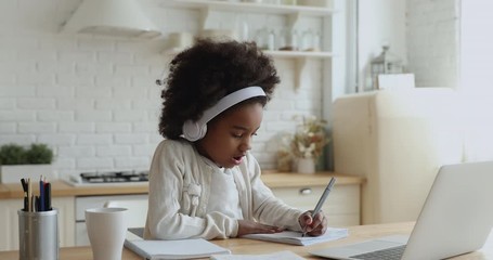 Cute african school girl elearning with online tutor at home. Mixed race child wearing headphones using computer app video calling watching online class lesson. Quarantine children education concept. - Powered by Adobe
