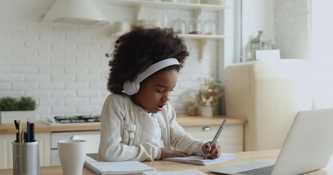 Cute african school girl elearning with online tutor at home. Mixed race child wearing headphones using computer app video calling watching online class lesson. Quarantine children education concept.