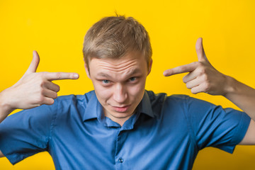 Smiling Young man pointing at blank.  in a blue shirt on a yellow background. It's me. select me....