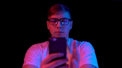 Young man with a smartphone. A man is using a telephone. Blue and red light falls on a man on a black background.