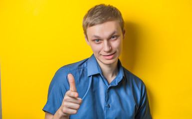 Blond young man shows his finger to the camera. Close portrait. Gesture. Isolated yellow background. photo