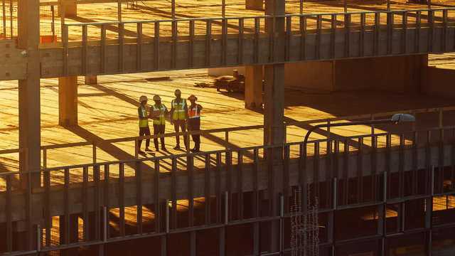 Aerial View: Diverse Team Of Specialists Inspect Commercial, Industrial Building / Skyscraper Formwork Construction Site. Real Estate Project Lead By Civil Engineer, Investor, Architect And Worker 