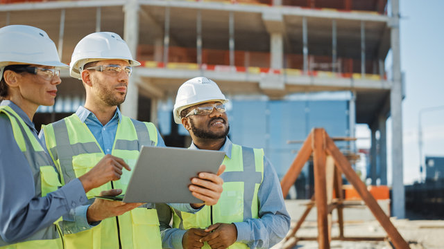 Diverse Team Of Specialists Use Laptop On Construction Site. Real Estate Building Project With Engineer Investor And Businesswoman Checking Area, Working On Civil Engineering, Discussing Strategy Plan