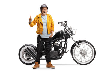 Mature biker in a yellow leather jacket standing with a chopper motorbike and showing thumbs up