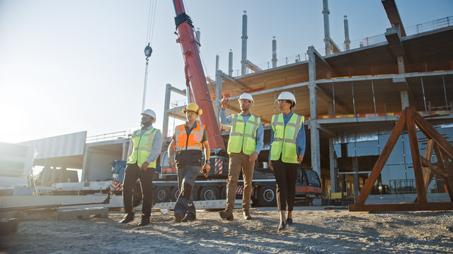Diverse Team of Specialists Inspect Commercial, Industrial Building Construction Site. Real Estate Project with Civil Engineer, Investor and Worker. In the Background Crane, Skyscraper Formwork Frames